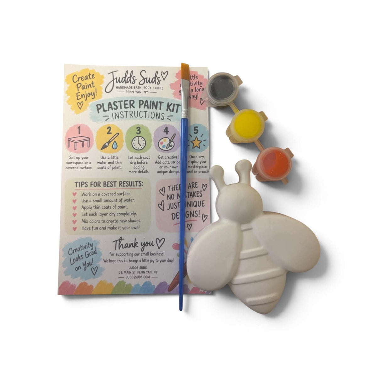 A children's plaster paint kit by Judd's Suds on a white background, including a printed instruction booklet, a blue paintbrush, five small paint pots, and a white bee-shaped plaster mold.