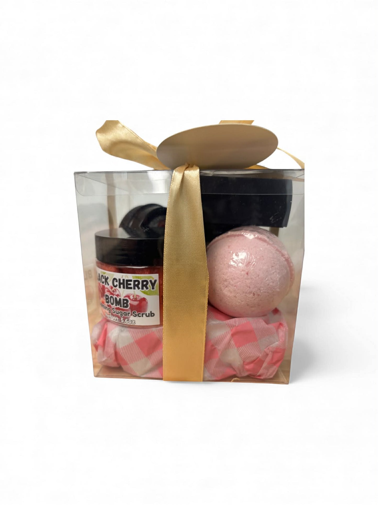 Gift set with bath bomb and scrub in a clear box with gold ribbon on a white background