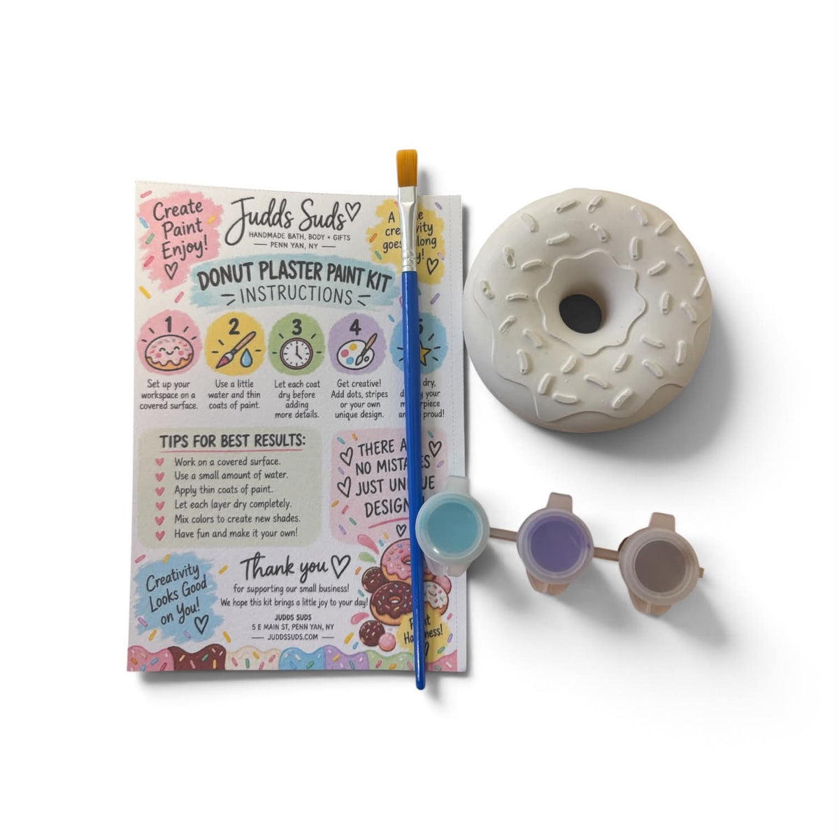 Fudd's Suds Donut Plaster Paint Kit shown with its instruction booklet, paint brush, three small paint pots, and a large donut-shaped plaster sample on a clean white background.