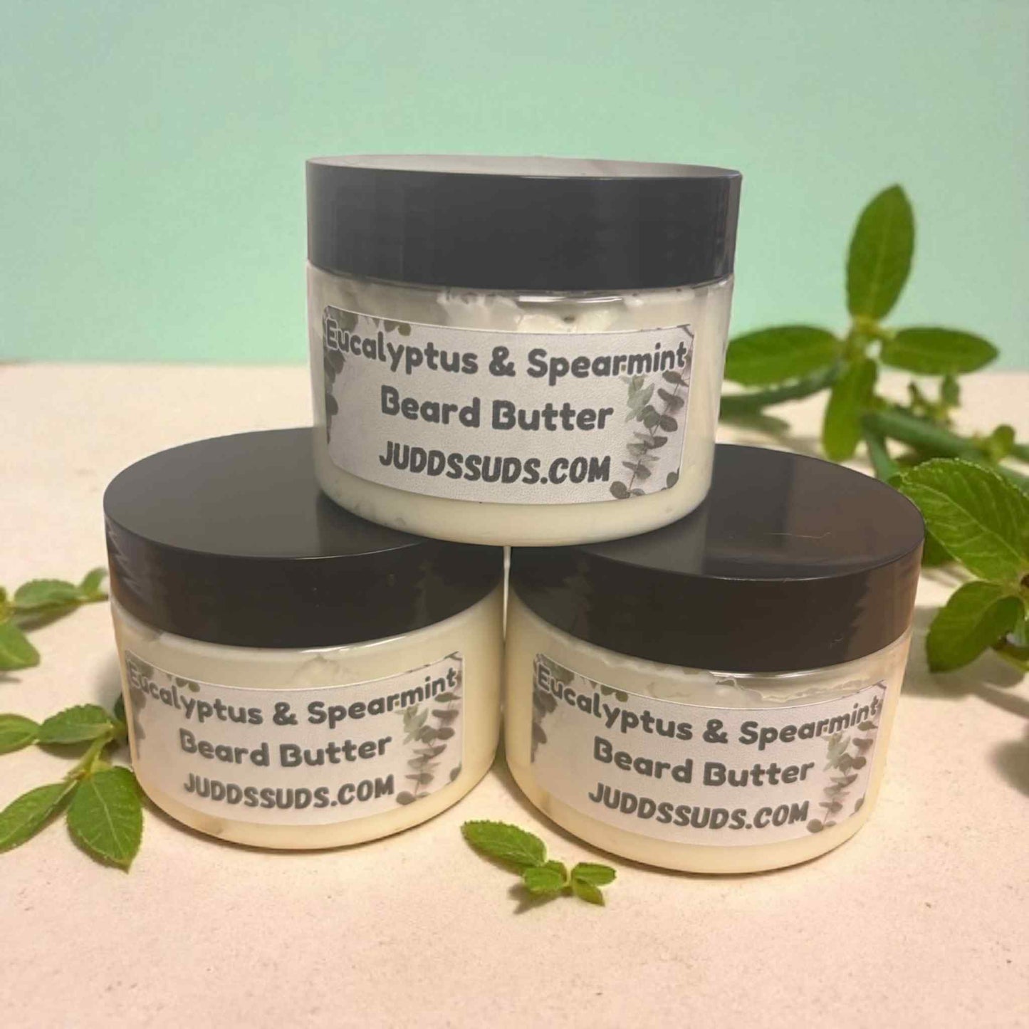 Three jars of Eucalyptus & Spearmint Beard Butter by Judds Suds on a light surface with greenery.