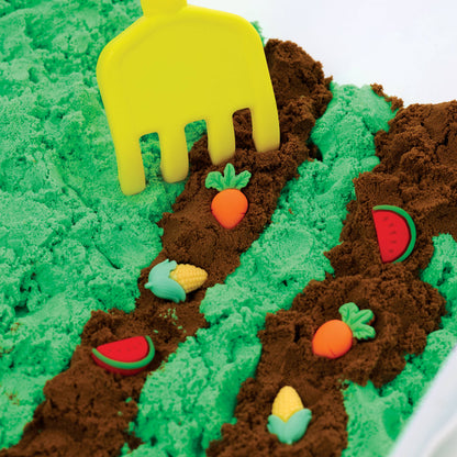 Play sand with green and brown sections, colorful vegetables, and a yellow tool on a white background