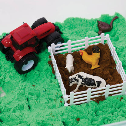Toy tractor and animals on a green sandy surface with a white fence.