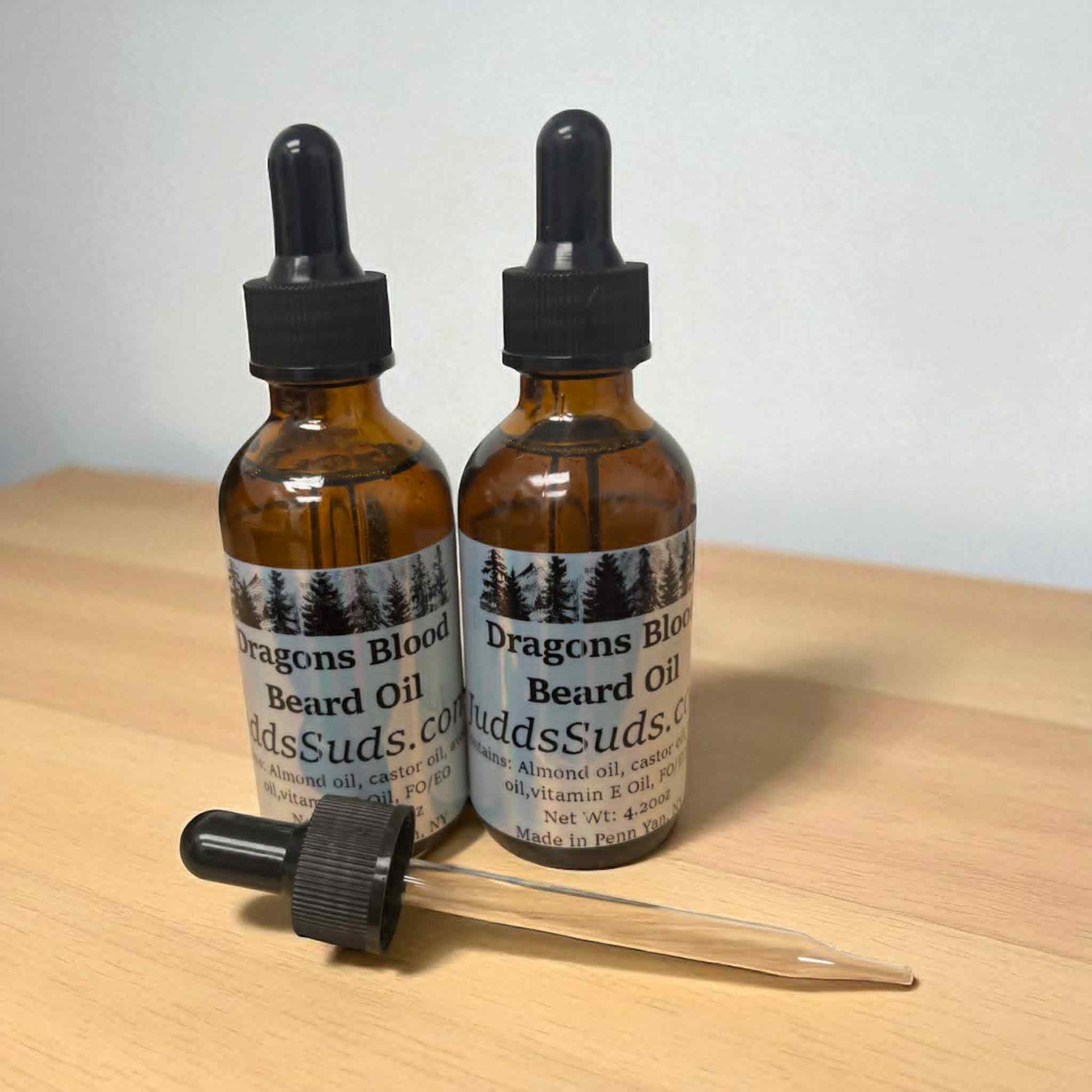 Two bottles of 'Dragon's Blood' beard oil with droppers on a wooden surface.