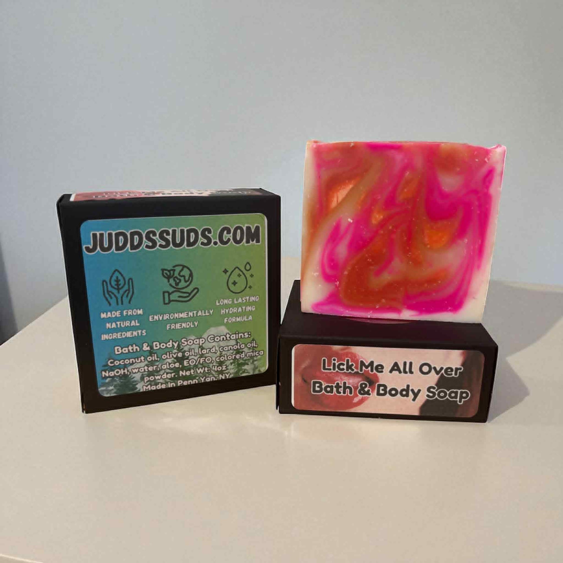 Bar of soap with pink and orange swirls next to a black box labeled 'JUDDSSUDS.COM' on a white surface.