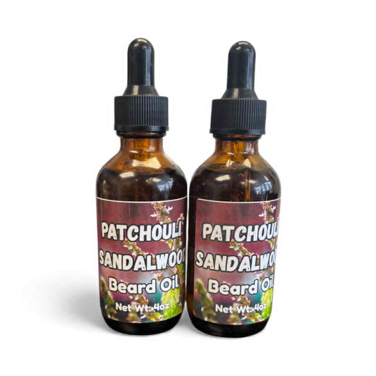 Two identical amber glass bottles with black dropper tops labeled ‘Patchouli Sandalwood Beard Oil,’ featuring a floral background design, standing upright against a white backdrop